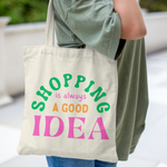 Canvas tote bag with colourful text that says “Shopping Is Always a Good Idea” – aesthetic reusable cotton bag held by a person in casual outfit outdoors
