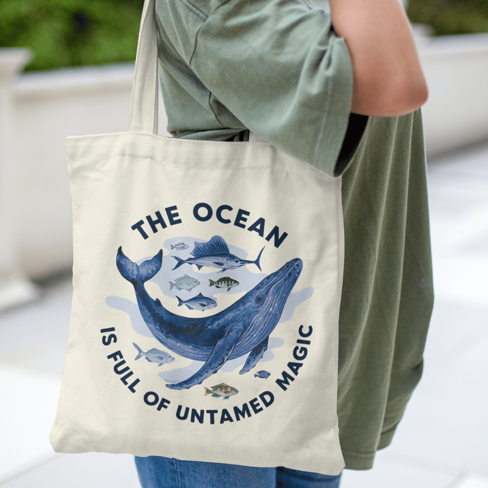 Eco-friendly organic cotton tote bag with whale and fish ocean design and “The Ocean Is Full of Untamed Magic” quote.