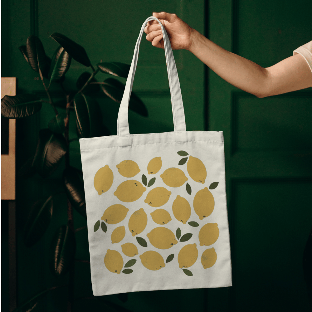 Organic cotton tote bag with a yellow lemon and green leaf all-over print design, reusable and eco-friendly.