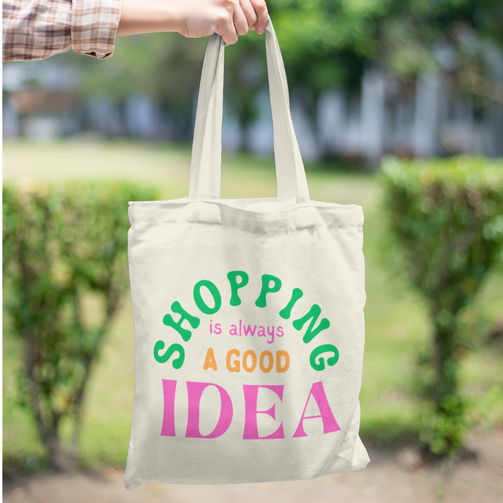 Canvas tote bag with colourful text that says “Shopping Is Always a Good Idea” – aesthetic reusable cotton bag held by a person in casual outfit outdoors