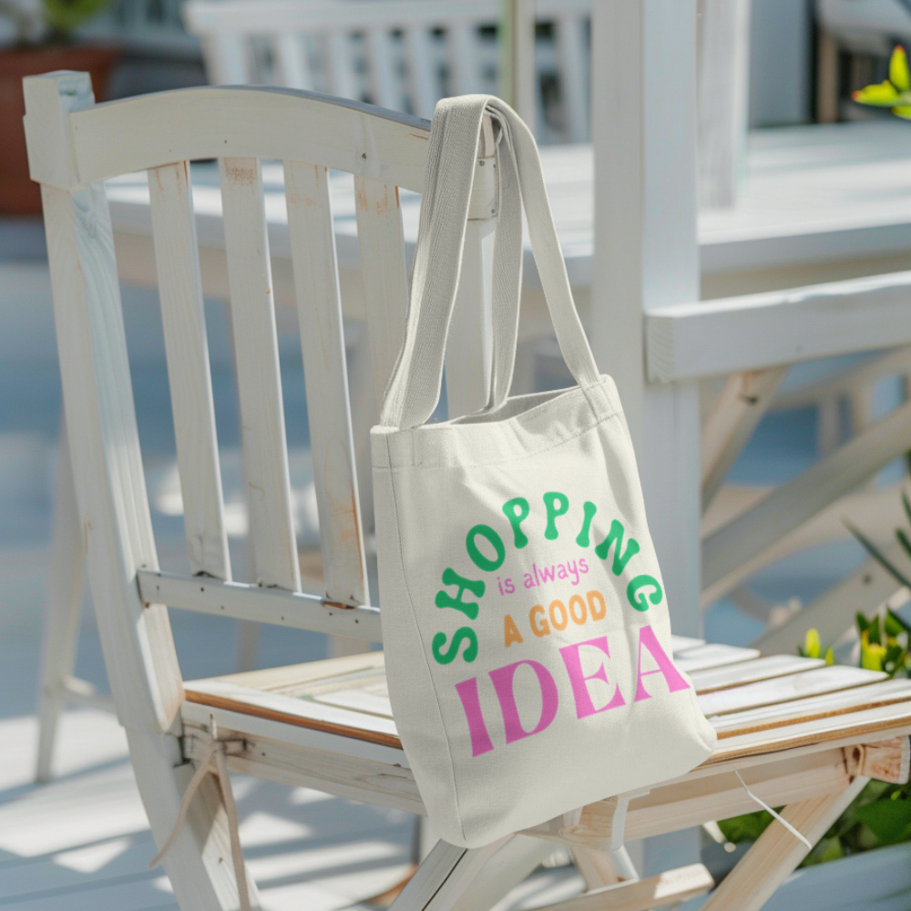 Canvas tote bag with colourful text that says “Shopping Is Always a Good Idea” – aesthetic reusable cotton bag held by a person in casual outfit outdoors
