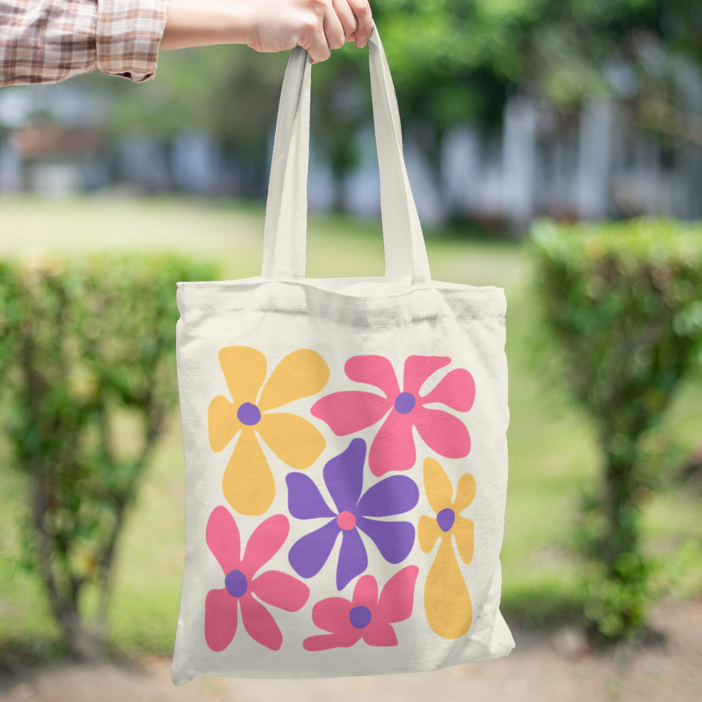 Tote bag with large colorful pink, yellow, and purple retro flowers – cotton canvas bag held by hand outdoors, groovy vintage style