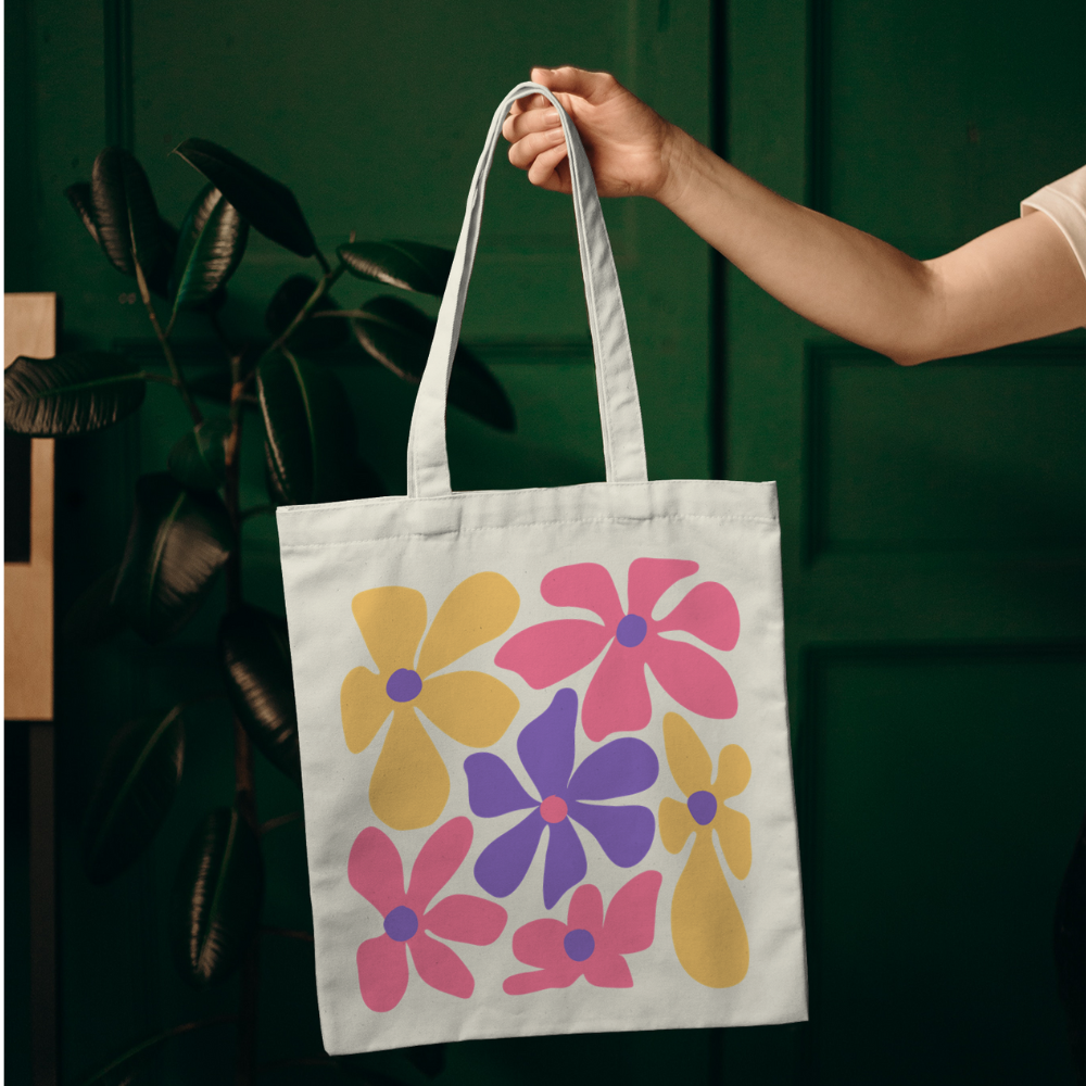 Tote bag with large colorful pink, yellow, and purple retro flowers – cotton canvas bag held by hand outdoors, groovy vintage style