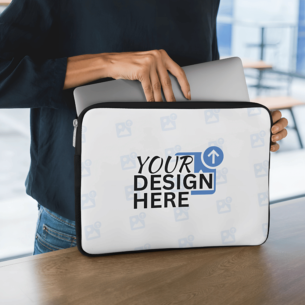 Person placing a laptop into a customisable white laptop sleeve with “Your Design Here” placeholder text in a modern workspace.