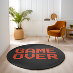 Round black rug with red pixel-style “GAME OVER” text, placed in a bright modern room with minimalist furnishings and warm neutral tones.
