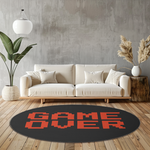 Round black rug with red pixel-style “GAME OVER” text, placed in a bright modern room with minimalist furnishings and warm neutral tones.