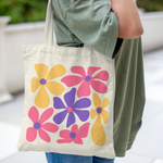 Tote bag with large colorful pink, yellow, and purple retro flowers – cotton canvas bag held by hand outdoors, groovy vintage style